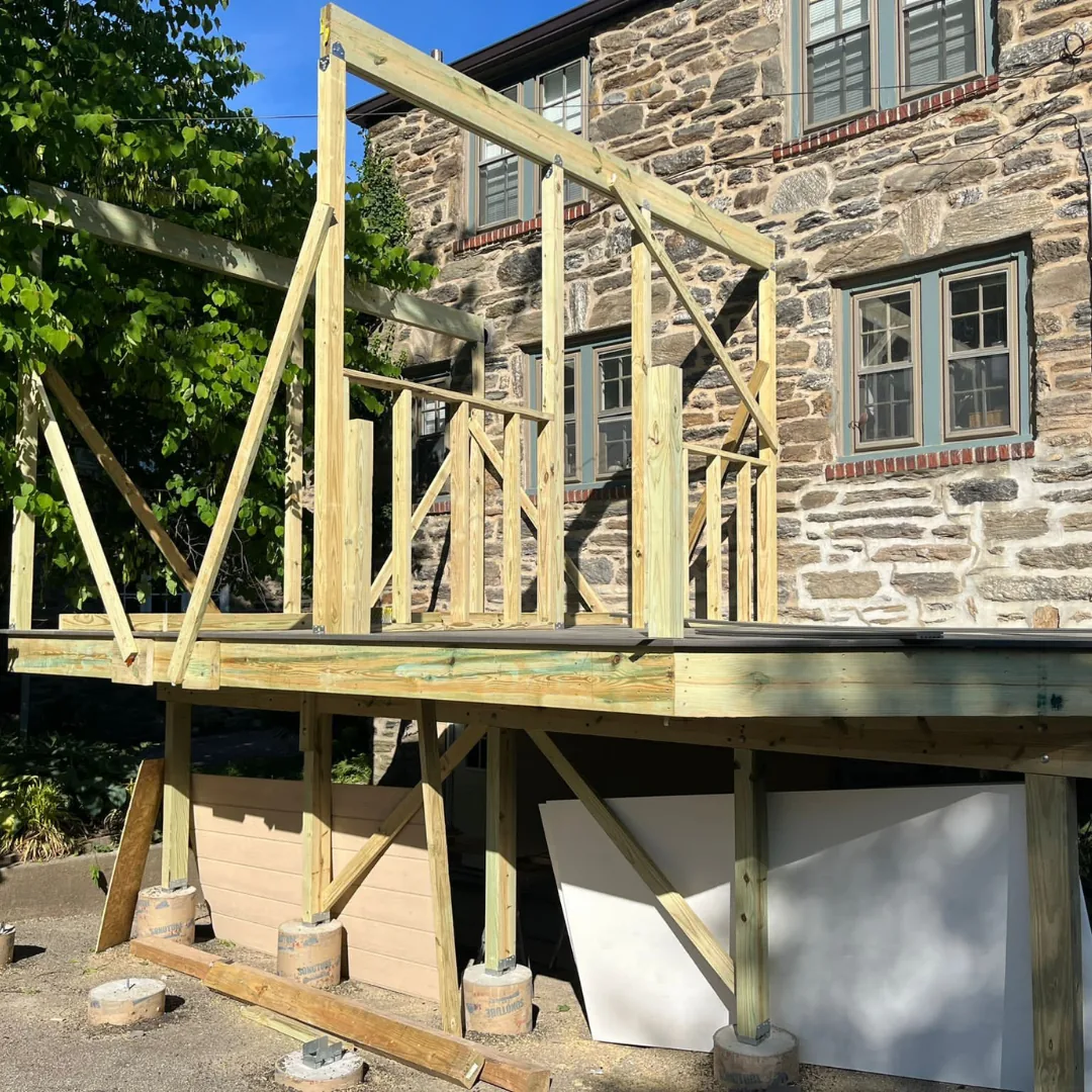 Deck framing under construction next to stone house.