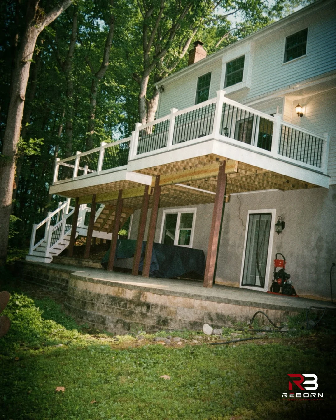 A newly constructed white deck with black railings on a house exterior. by Reborn General Construction LLC in Ambler, PA