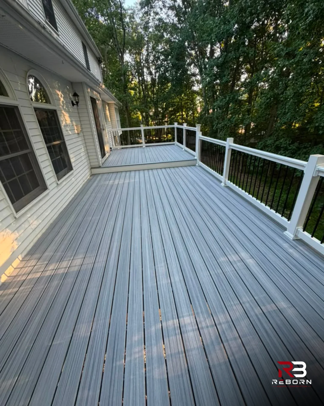 Newly built composite deck with gray planks and white railings, attached to a house. by Reborn General Construction LLC in Do