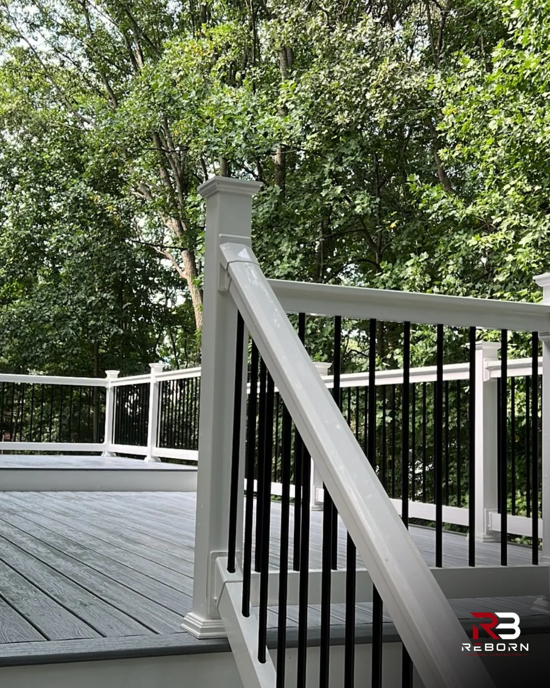 Newly built deck with gray composite decking, white railings, and black balusters. by Reborn General Construction LLC in Doyl
