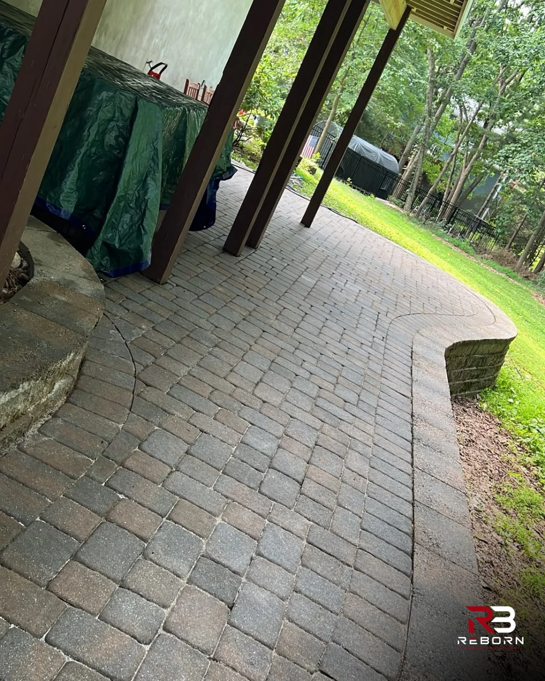 Beautiful new paver patio and retaining wall under a deck, surrounded by trees. by Reborn General Construction LLC in Newtown